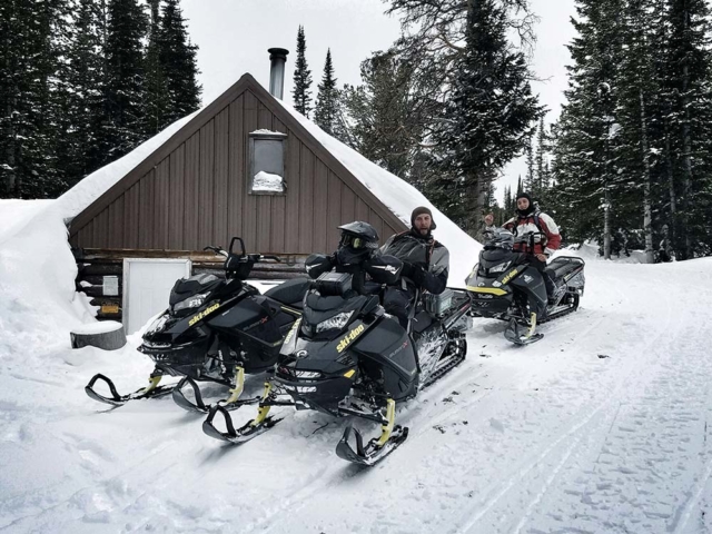 group of snowmobilers trail riding in montana with building behind
