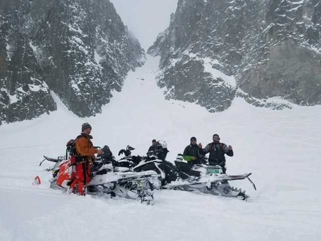 snowmobilers trail riding in montana below powder couloir