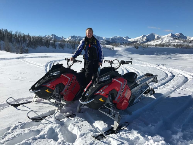guy standing by snowmobiles while snowmobiling in montana